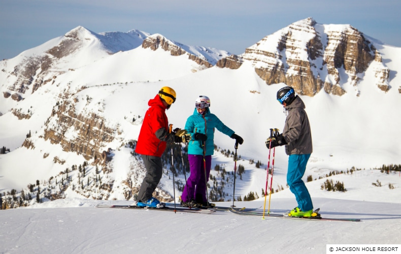 3 skiers having a conversation before descending the mountain