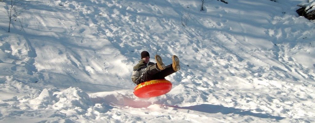 A man on a snow tubing run launches into the air going over a bump